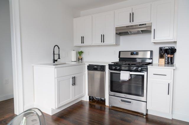 guest post 06262025 Compact white kitchen with stainless steel appliances and dark wood flooring in a modern guest house